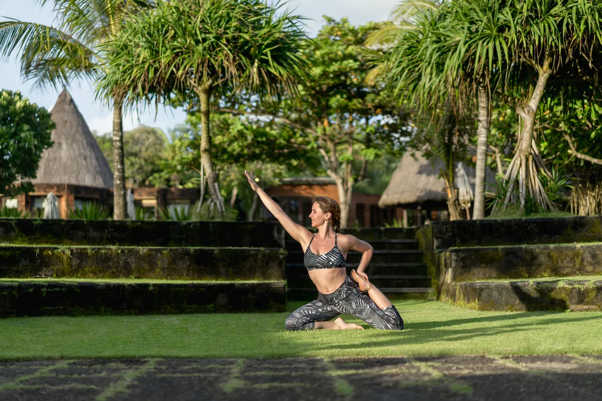 Pratique de yoga dans un jardin tropical avec toits de chaume traditionnels balinais près d'Ubud
