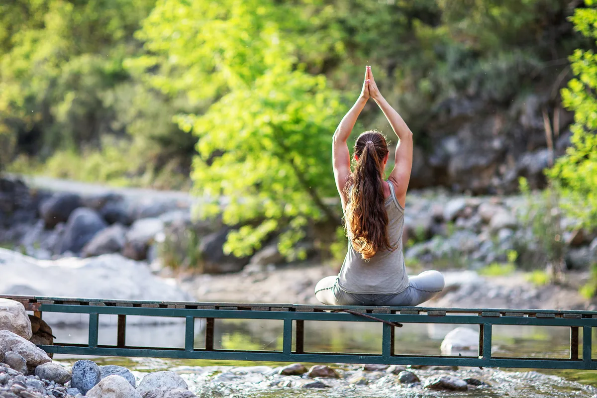 Femme en méditation sur une passerelle au-dessus d'une rivière verte bordée de forêt dans le nord de l'Inde